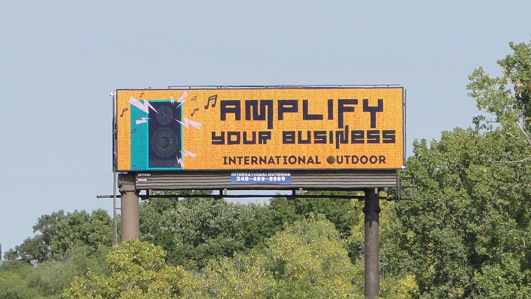 A photo of a billboard above the tree line with a message that reads "Amplify Your Business"